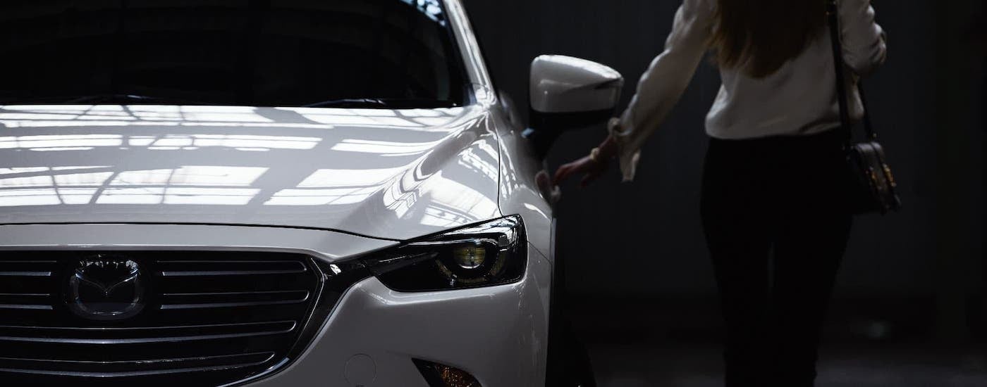 A woman is about to open the door to a white 2021 Mazda CX-3 at a Houston Mazda dealership, shown from the front.