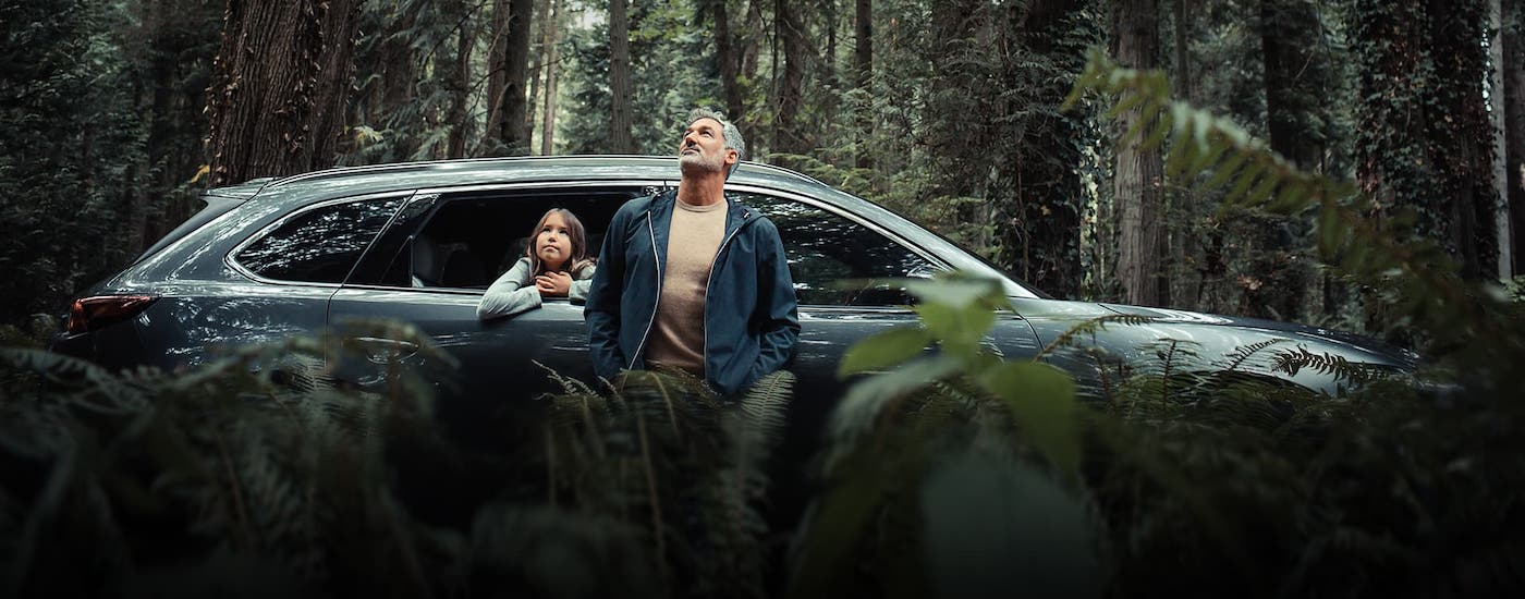 A man and child are looking at the forest in front of a gray 2021 Mazda CX-9 that is parked in the woods.