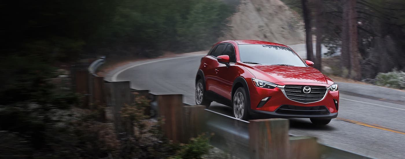 A red 2020 Mazda CX-3 from a Mazda dealer near you is driving around a winding forest road.