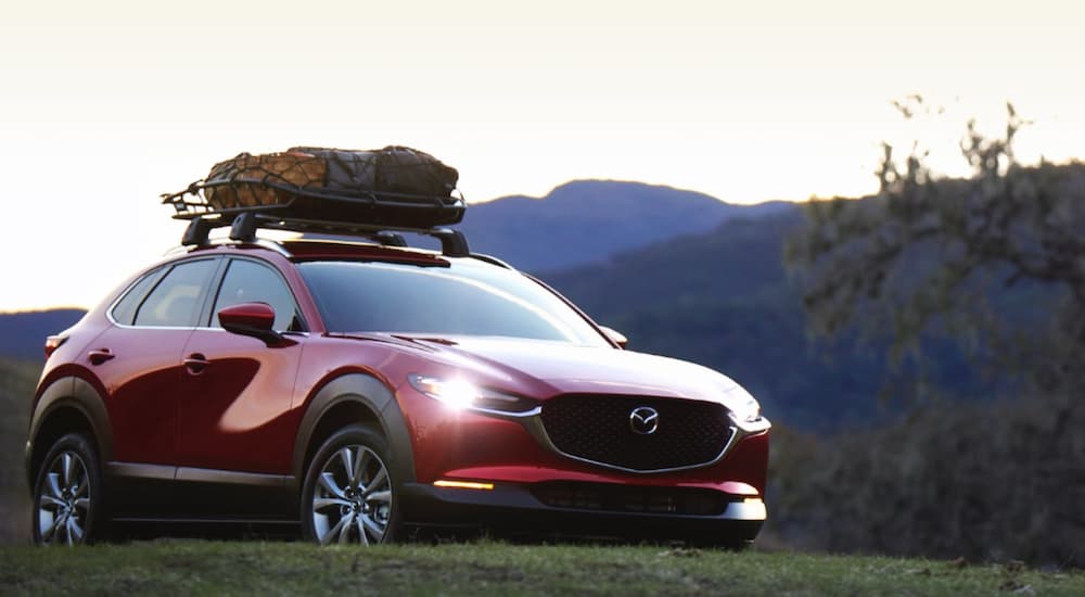 A red 2021 Mazda CX-30 is parked in front of mountains with luggage on the roof at dusk after leaving a Mazda dealer near me.