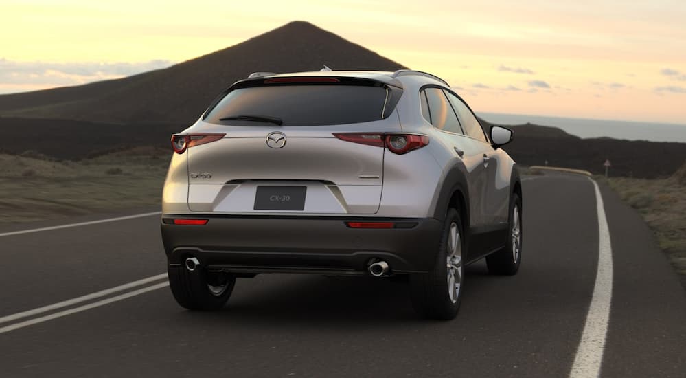 A silver 2021 Mazda CX-30 is shown from the rear in front of a mountain at sunset.