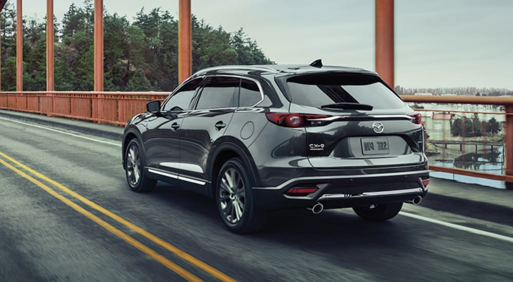 A grey 2021 Mazda CX-9 is shown from the rear driving across a bridge.