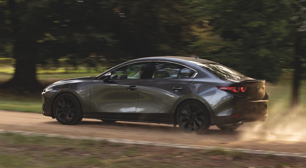 A silver 2021 Mazda3 is shown from the side driving down a dirt road.