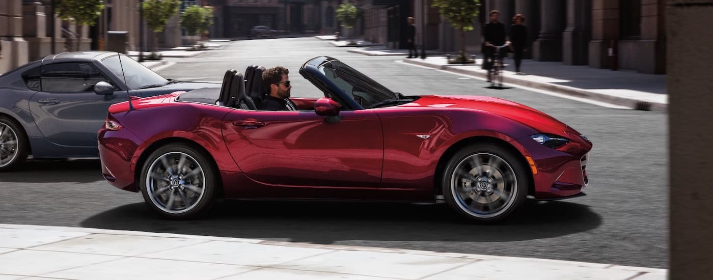 A red 2021 Mazda Miata MX-5 is shown from the side driving in a city.