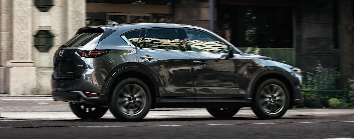 A black 2021 Mazda CX-5 is shown from the side driving on a city street.