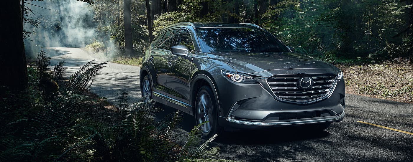 A gray Mazda CX-9 is driving on a woodland road.