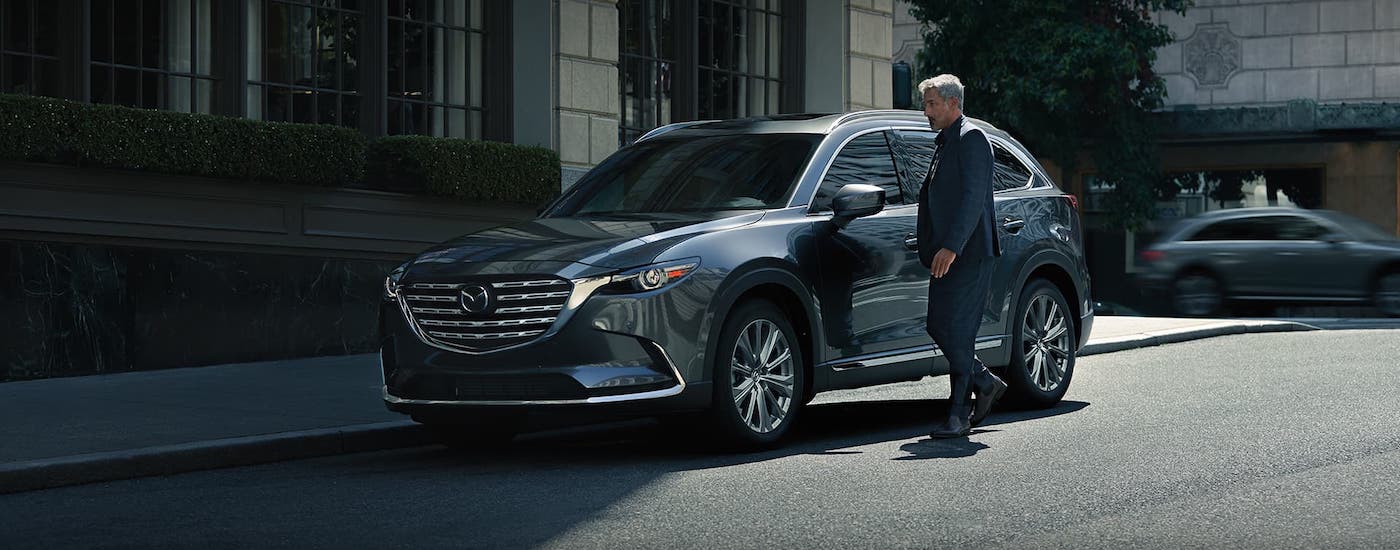 A man is walking towards a gray 2021 Mazda CX-9 that is parked in front of a city building.