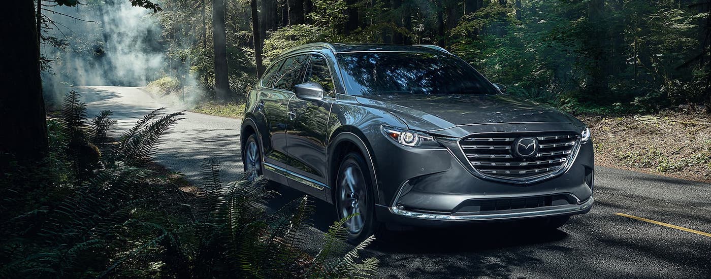 A gray 2021 Mazda CX-9 is driving on a misty woodland road.